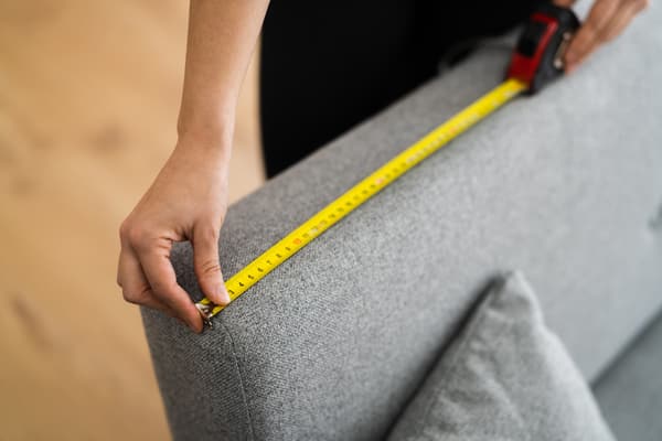 A close-up of a person measuring the back of a sofa
